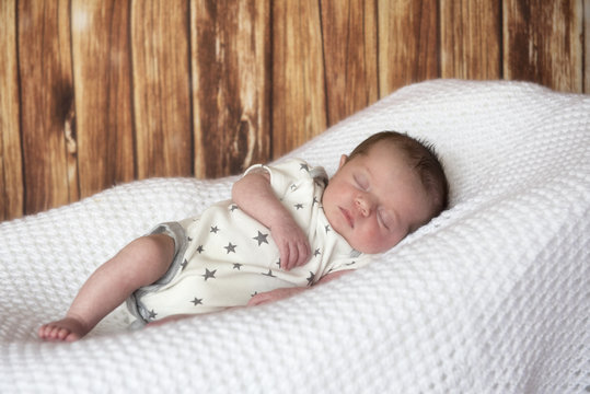 Portrait image of a new born baby boy, laying on a white blanket, with a wooden effect background. 