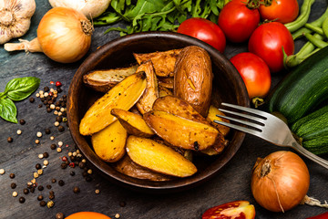 Roasted potatoes with herbs and vegetables on rustic background