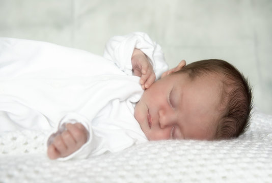 Close up portrait image of a new born baby boy, laying on a white blanket. 