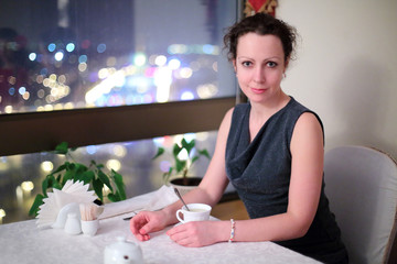 Beautiful woman sitting at table by the window in the restaurant in the evening