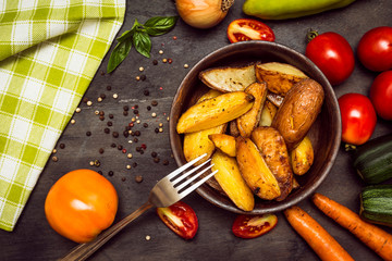 Roasted potatoes with herbs and vegetables on rustic background