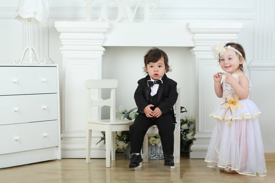Beautiful little girl in white long dress plays with small boy in black tuxedo