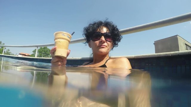 Happy woman drinking frape caffee by swimming pool