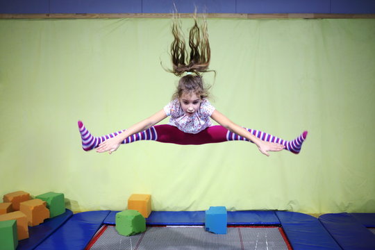 Girl is jumping high in striped tights on the big trampoline.