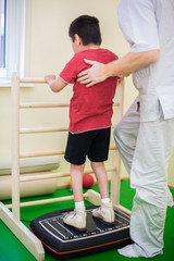 physician supports a child standing on the training platform
