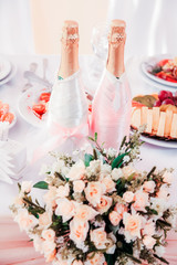 
Two decorated champagne bottle stand on urashennom table with a bouquet of flowers