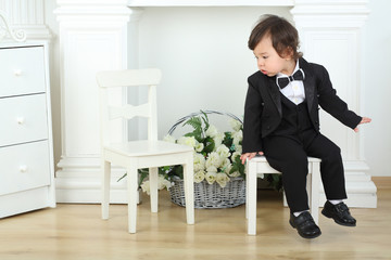 Little boy in black suit sitting on white chair and looks at next chair