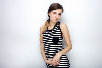 Portrait of cute young beautiful woman in striped shirt touching her elbow posing for model tests against studio background