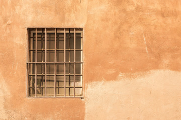 A window, with iron bars, set into an ochre colored stone wall - Rome Italy 