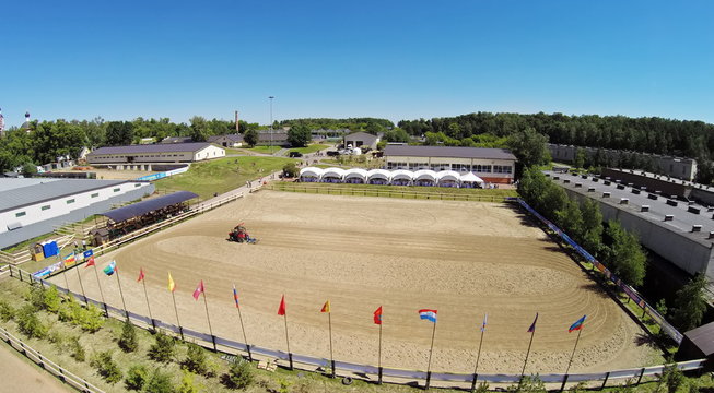 Tractor prepares sand on equestrian arena of sports complex Sozidatel before Russian Championship for Dzhigitovka at sunny summer day. Aerial view. Photo with noise from action camera.