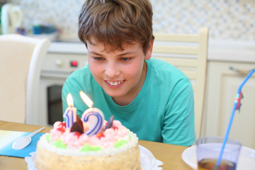 Happy boy makes a wish before blow out a candle on a birthday cake in the kitchen
