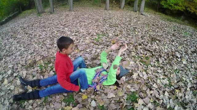 Two children play in fall park throwing leaves and wrestling, 
