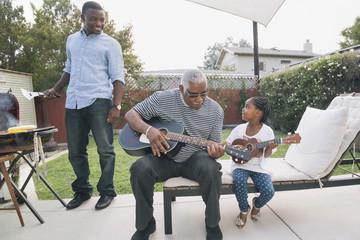 African American grandfather teaching granddaughter to play guitar