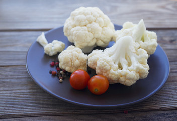 Fresh cauliflower and cherry tomatoes on a brown round plate on a wooden surface close up, soft focus