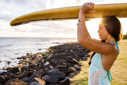 Pacific Islander surfer carrying surfboard on rocky beach
