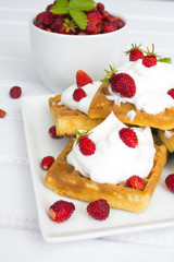 waffles with wild strawberries and whipped cream on white table