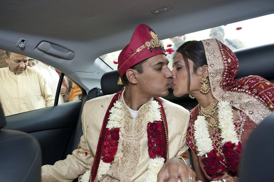 Indian bride and groom in traditional clothing kissing in car