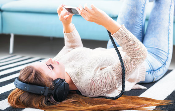 Woman with headphones lying and listening to music at home