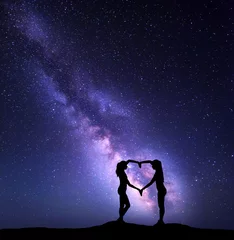 Fototapete Rund Girls holding hands in heart shape on the background of the colorful Milky Way. Night landscape with starry sky. Amazing galaxy. Silhouette of women © den-belitsky
