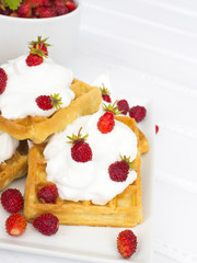 waffles with wild strawberries and whipped cream on white table
