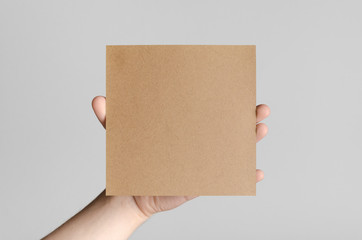 Kraft Square Flyer / Invitation Mock-Up - Male hands holding a kraft flyer on a gray background.