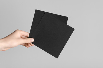Black Square Flyer / Invitation Mock-Up - Male hands holding black flyers on a gray background.