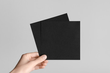 Black Square Flyer / Invitation Mock-Up - Male hands holding black flyers on a gray background.