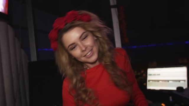 Dj girl in red dress dance at turntable in nightclub with headphones. Smile. Red rim on head