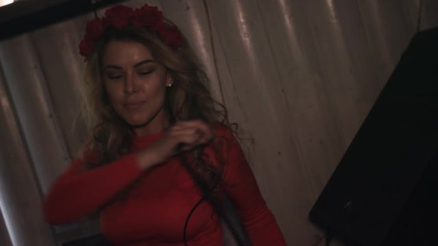 Dj girl in red dress dance with headphones at turntable in nightclub. Red flower rim on head.