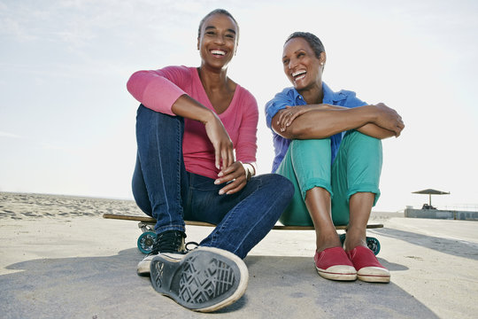 Older Black Women Sitting On Skateboard On Beach