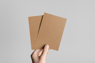 Kraft A6 Flyer / Postcard / Invitation Mock-Up - Male hands holding blank flyers on a gray background.