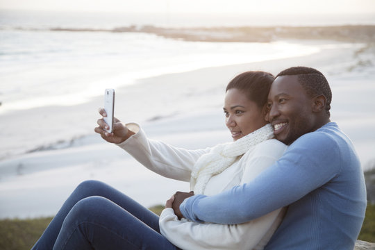 Smiling couple taking cell phone selfie at beach