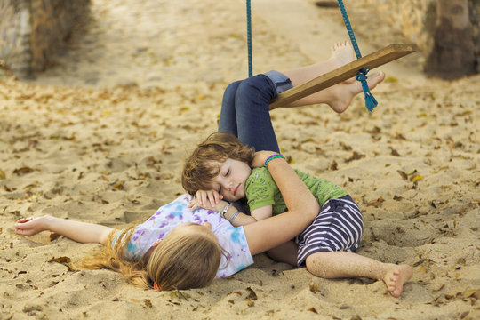 Caucasian boy laying on chest of sister at beach