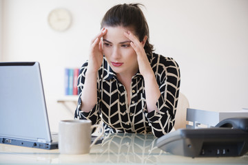 Caucasian businesswoman with headache using laptop