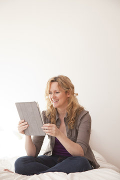 Caucasian woman sitting on bed using digital tablet