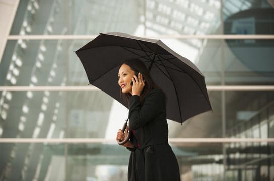 Smiling businesswoman with umbrella talking on cell phone