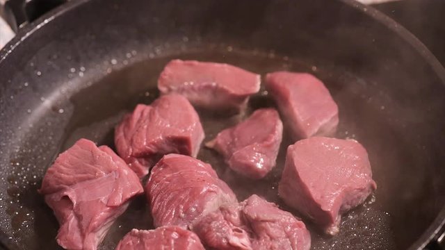 Frying beef sirloin in a hot pan. Pieces of  beef meat - close-up on top of a kitchen tile.