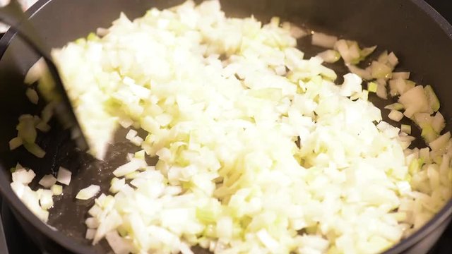 Chopped onions fried in vegetable oil in the pan. Close-up on top of a kitchen tile. 