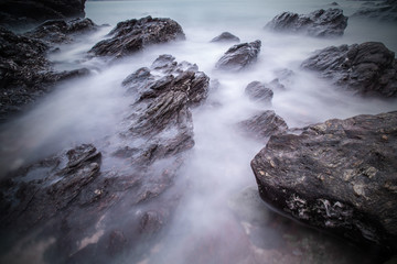 Soft waves of ocean in sunset with stones on the beach backgroun