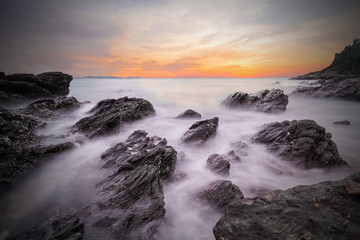 Soft waves of ocean in sunset with stones on the beach foregroun