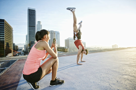 Woman photographing man doing handstand on urban rooftop
