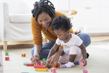 Black mother and baby daughter playing with blocks on carpet