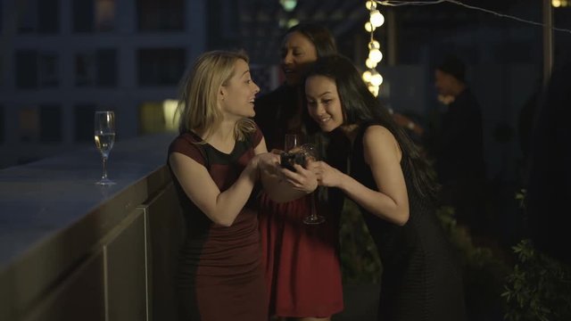  Happy female friends pose to take a selfie at summer rooftop party