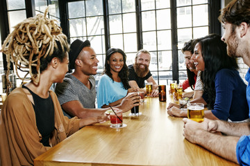 Smiling friends drinking at table in bar