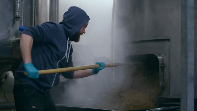  Worker in a brewery removing mash from the bottom of a machine
