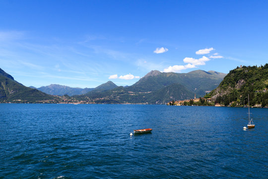 View towards Lake Como with boats and village Varenna with mountains in Lombardy, Italy