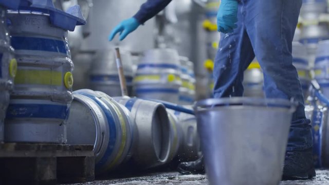  Low angle view worker in a brewery filling barrels of beer with a hose