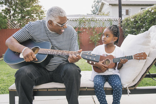 African American grandfather teaching granddaughter to play guitar