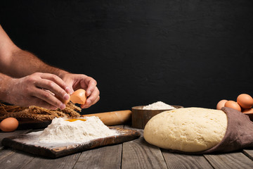 Male hands break the egg into flour for making bread