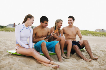 Teenagers sitting on surfboard and playing ukulele on beach